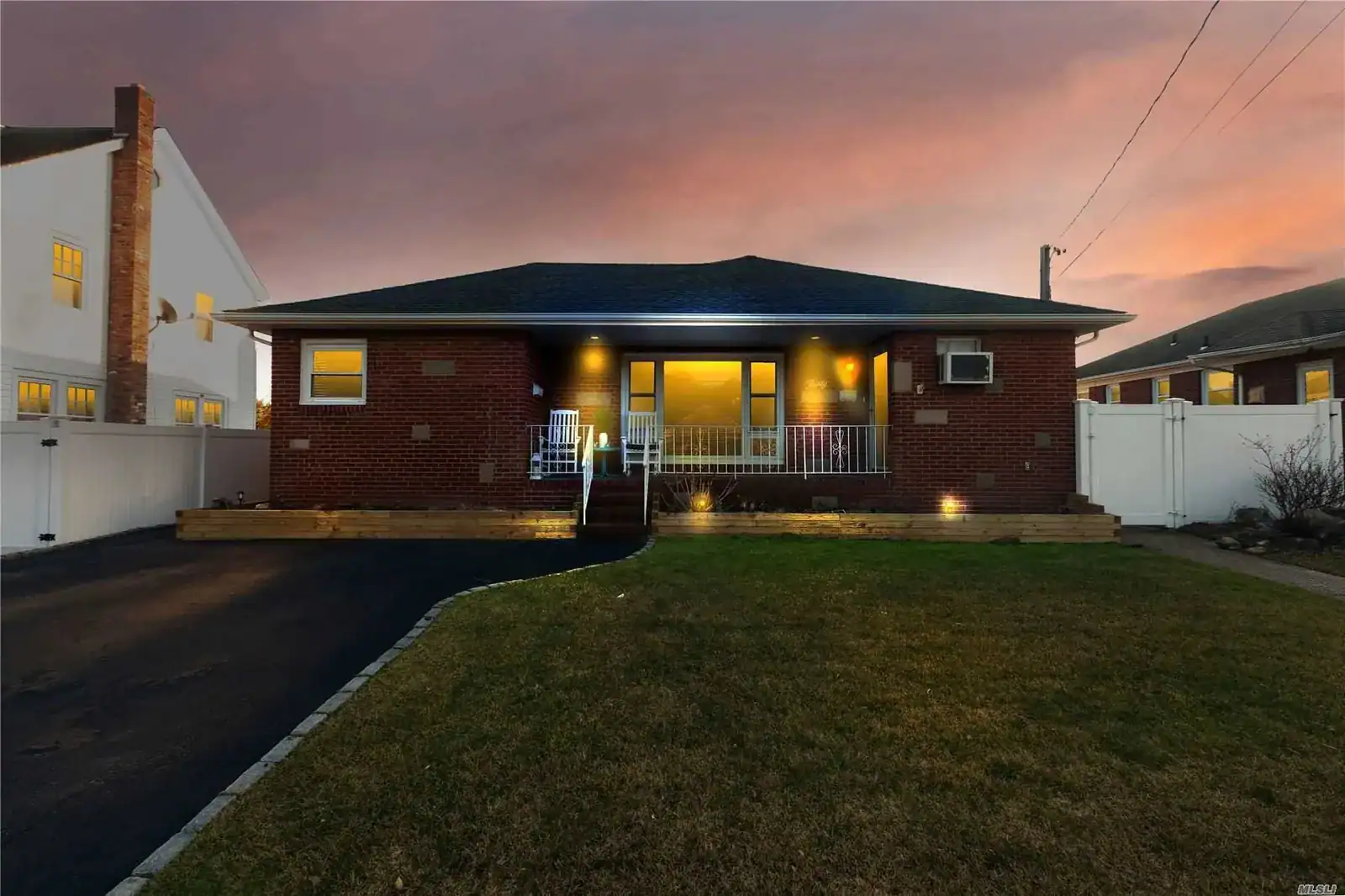 Brick house with front porch and outdoor lighting at sunset.